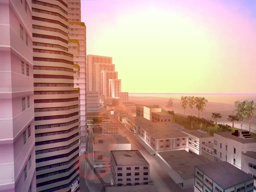 Looking down past a row of pastel hotel towers toward a palm lined beach and the sea in hazy sunset light