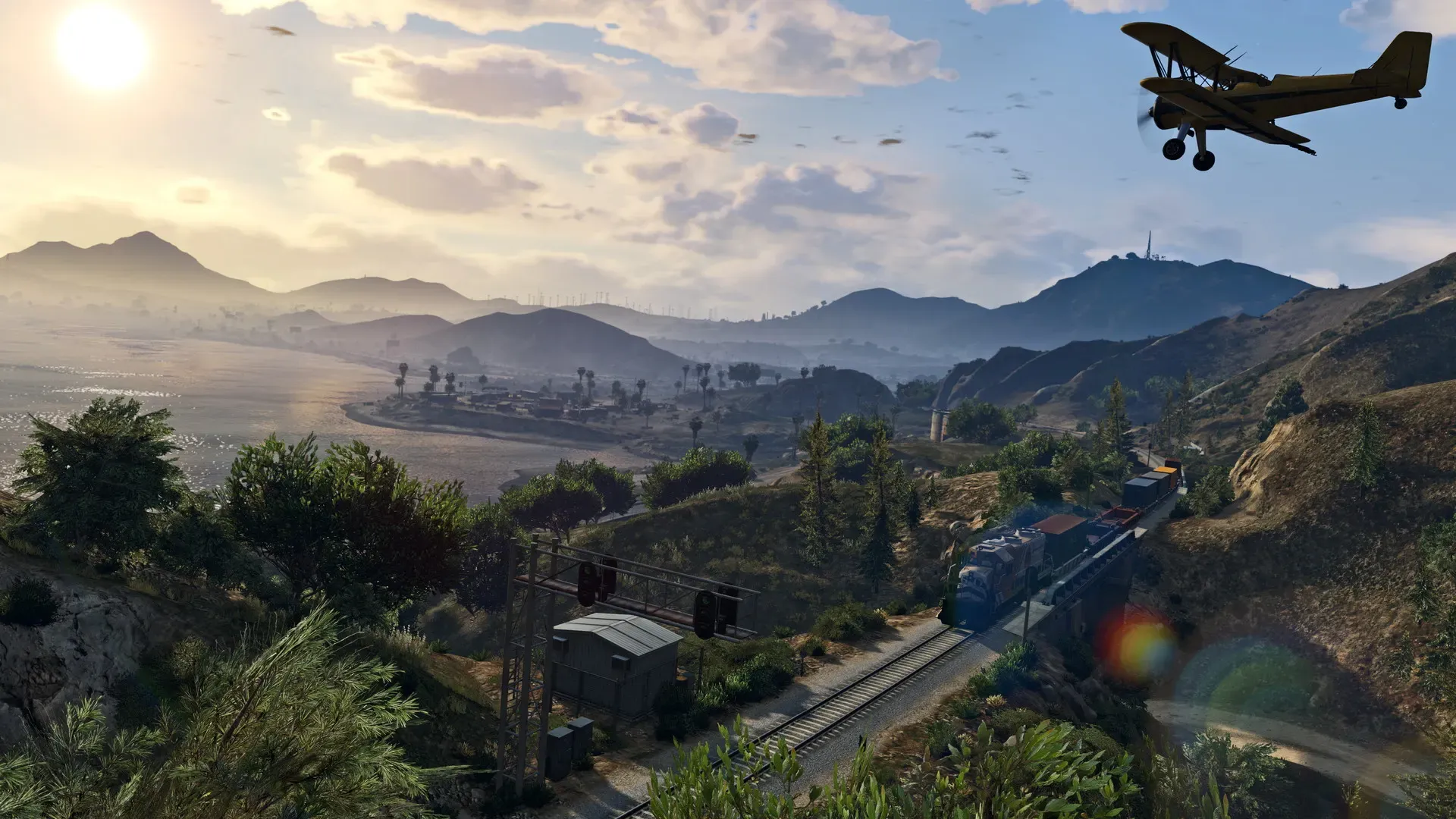 A crop duster plane flies over green hills as a freight train runs along a valley toward the sea