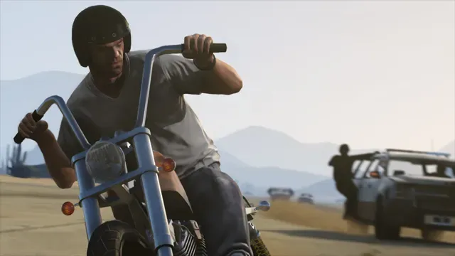 A helmeted rider on a chopper motorcycle flees across the desert as police take cover behind a car