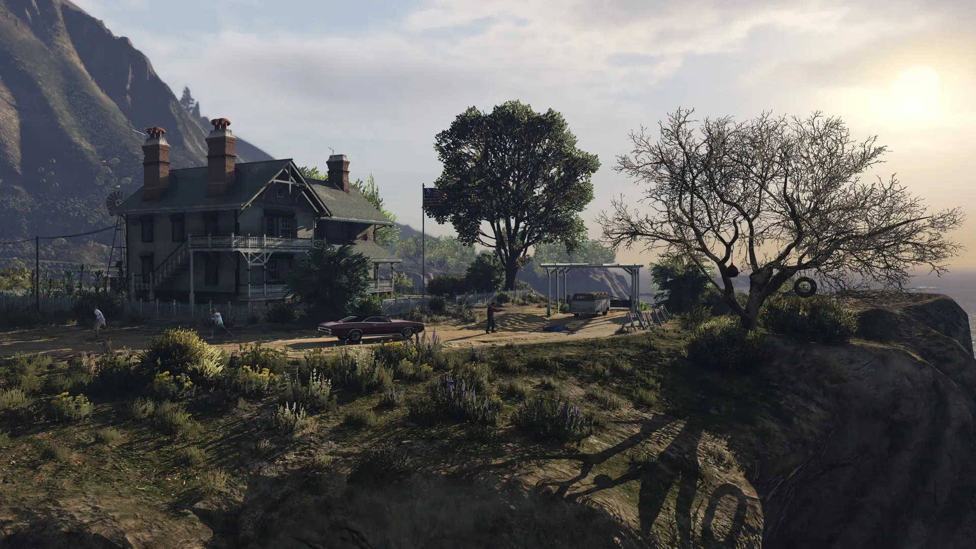 An old two storey house with chimneys on a grassy clifftop, with a tree and a tyre swing in the evening light