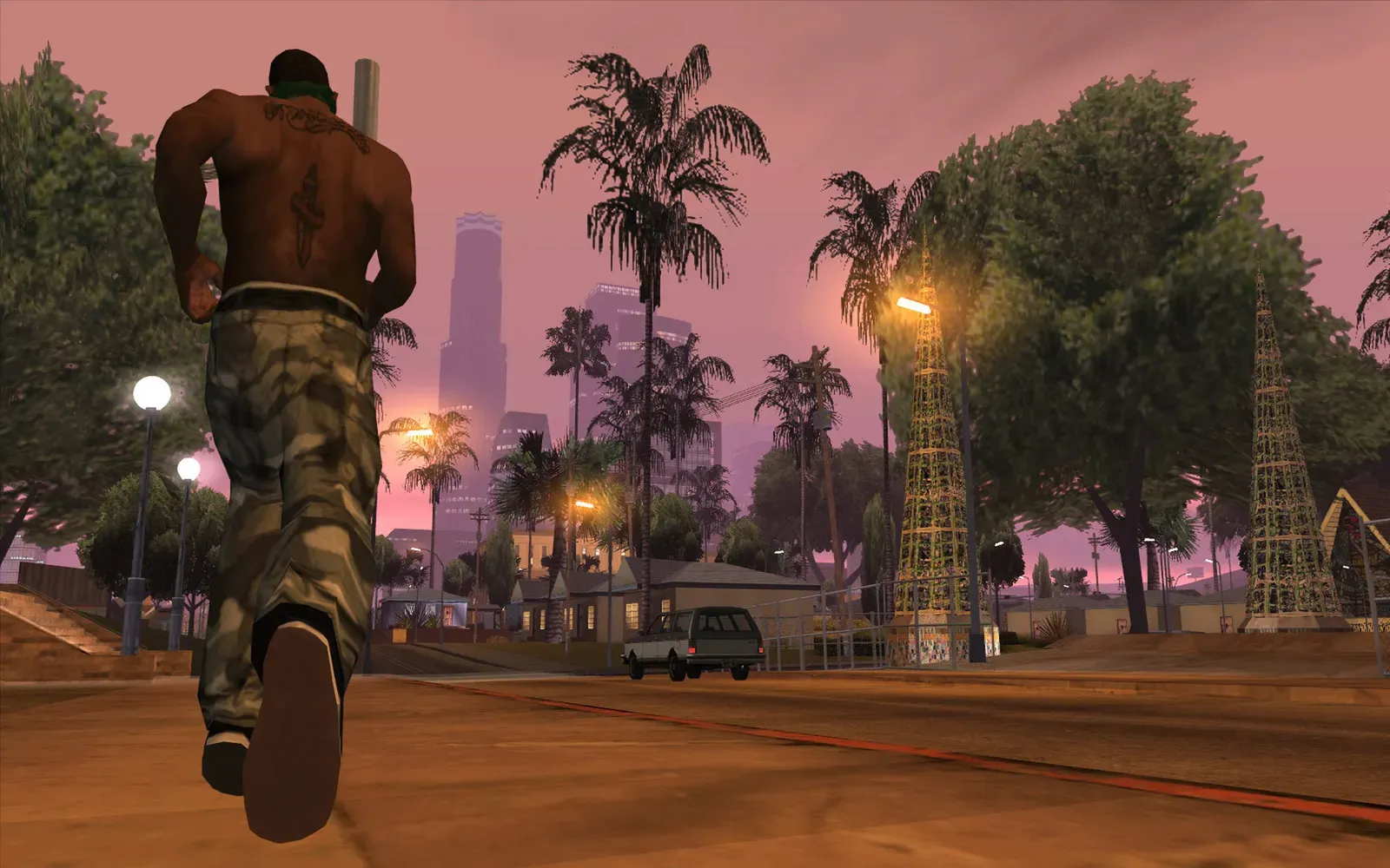 Original game (PC): a shirtless man in camouflage trousers runs along a street toward the downtown Los Santos towers under a pink dusk sky