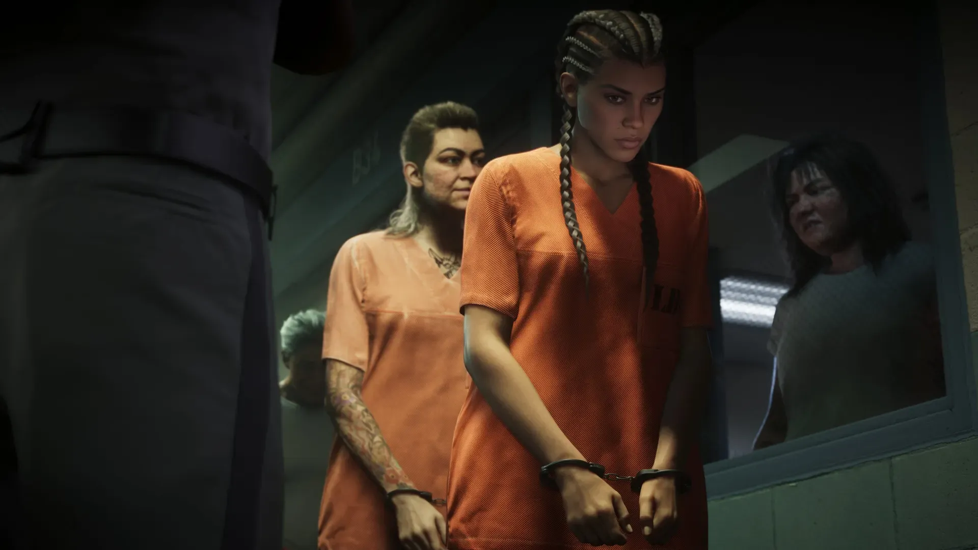 Inside a jail, Lucia and another woman are handcuffed and wearing orange jumpsuits as they walk by a window where another woman watches through the glass. An officer stands nearby.