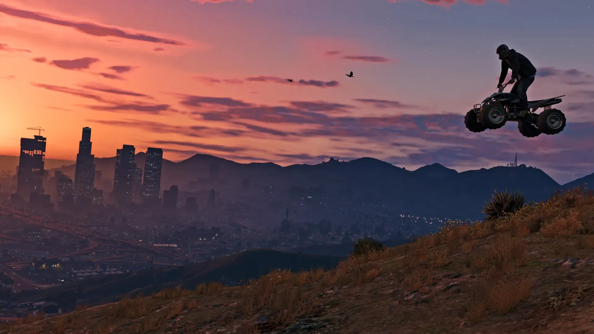 A rider jumps a quad bike off a hilltop as the Los Santos skyline glows under a pink sunset