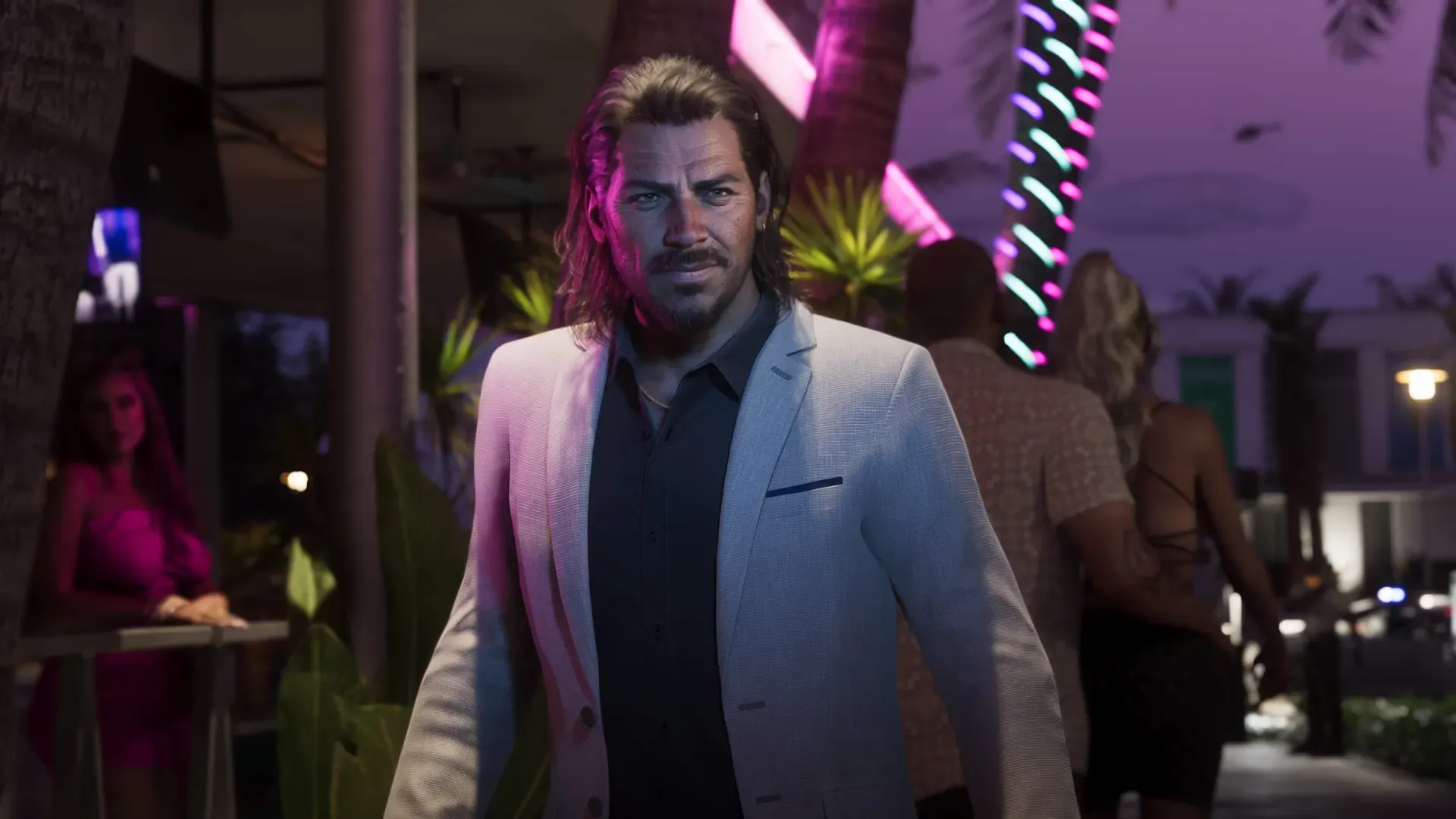 Raul wearing a suit looks off into the distance. In the background people walk down a neon-lit sidewalk.