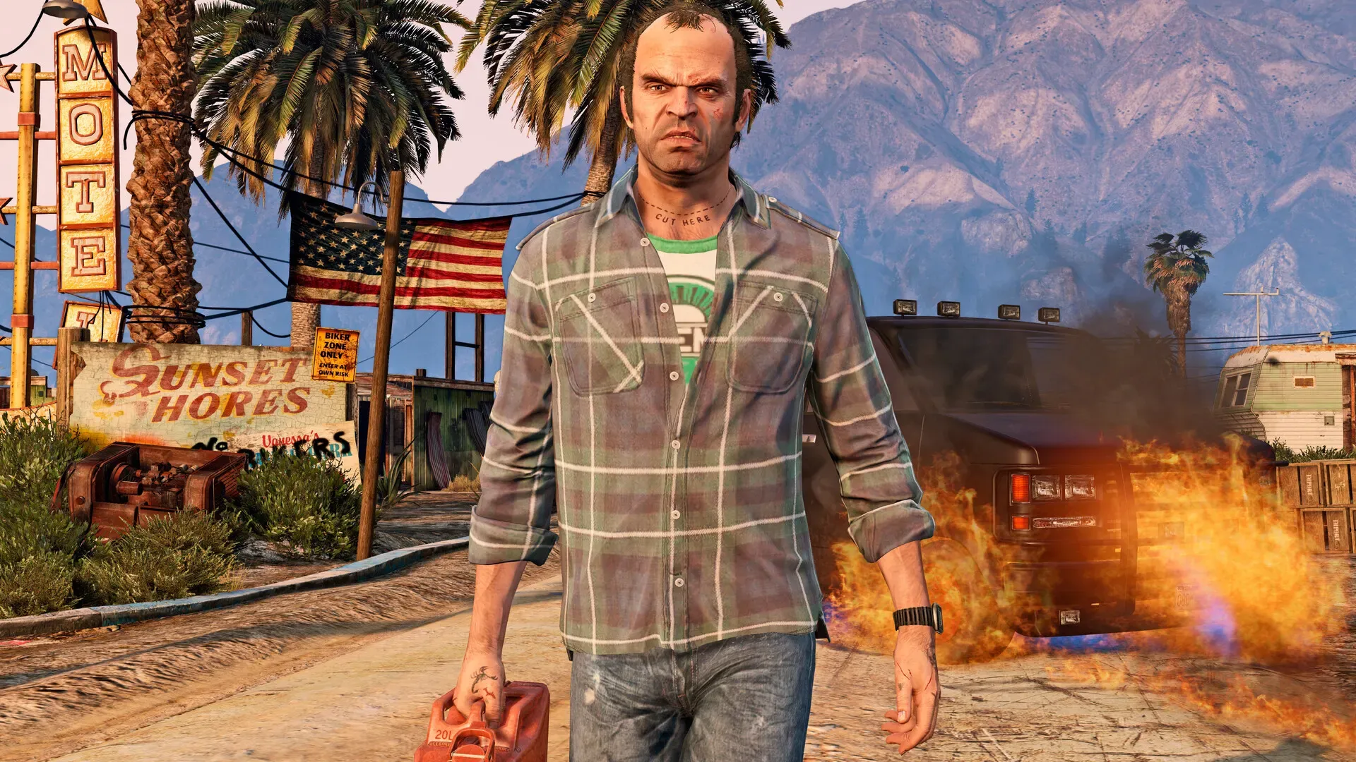 Trevor walks away from a burning vehicle carrying a fuel can, outside a run down motel in the desert