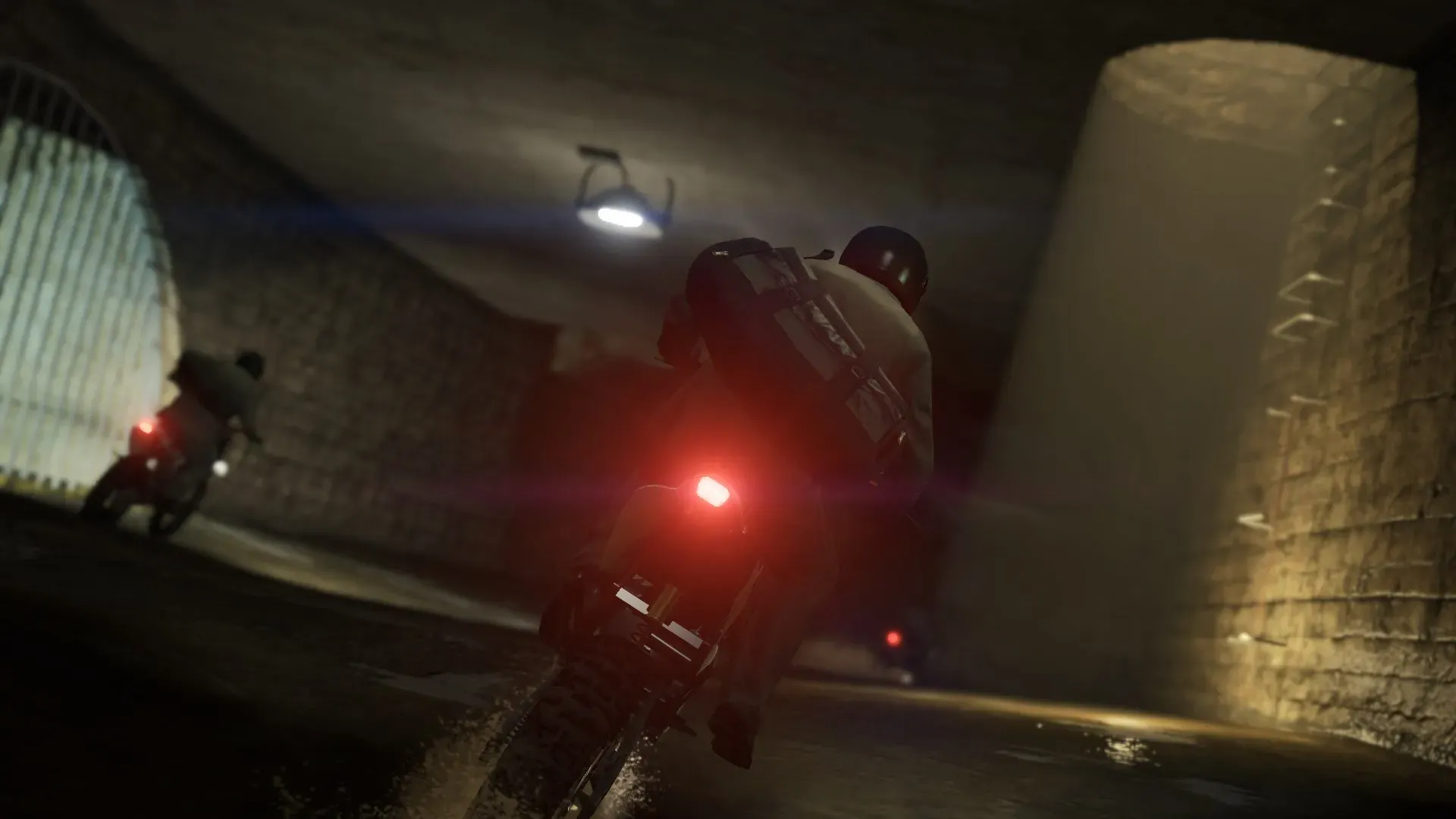 A motorcyclist with a backpack chases another rider through a dim concrete tunnel