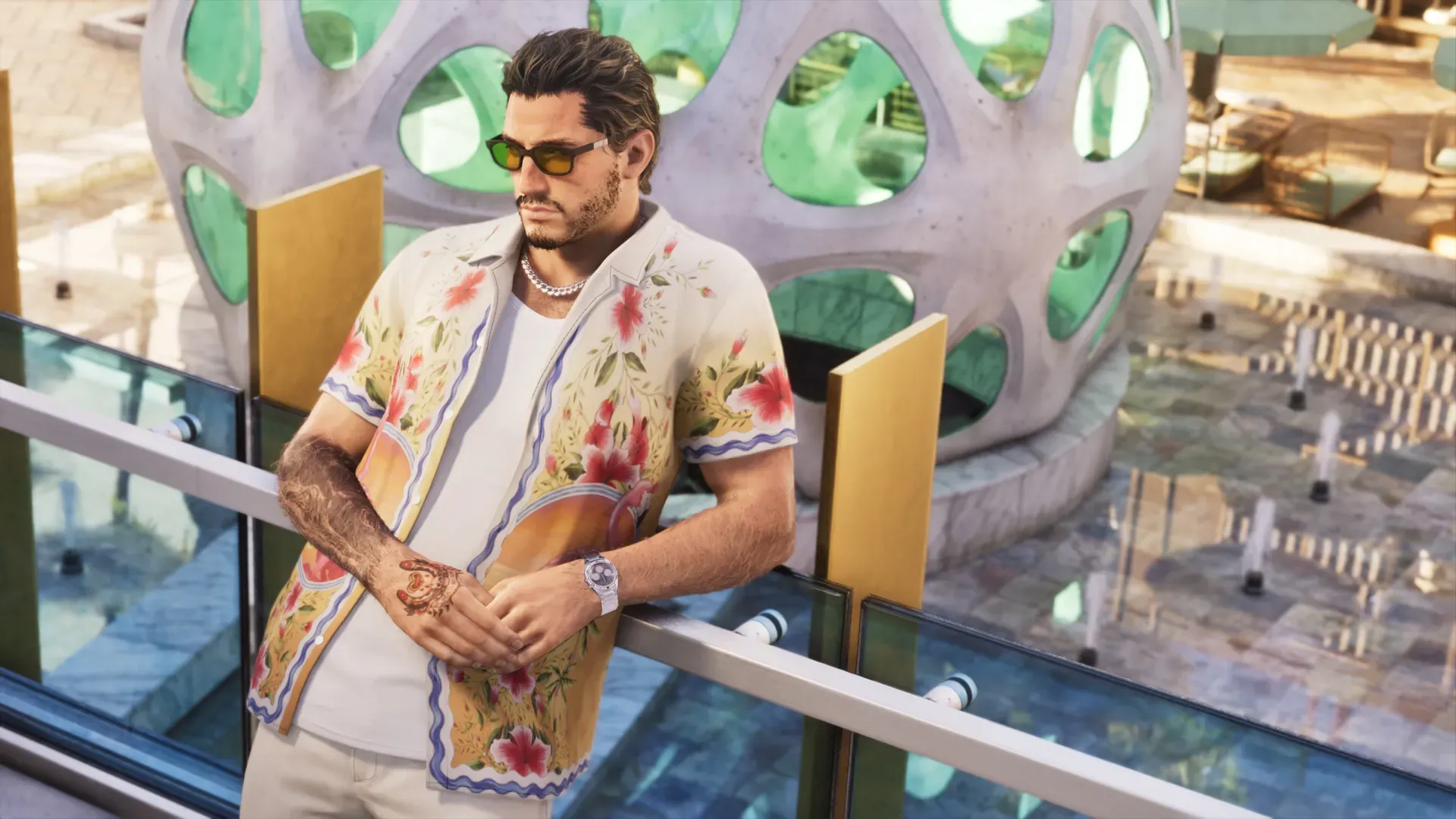Jason leaning on a ledge, wearing an open button down shirt with a tropical pattern, along with sunglasses.